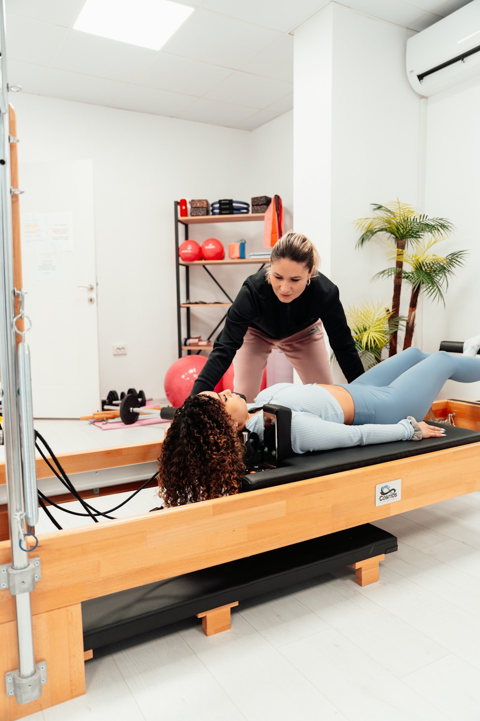 Pilates eğitmeni ahşap reformer makinesinde danışanına rehberlik ediyor.