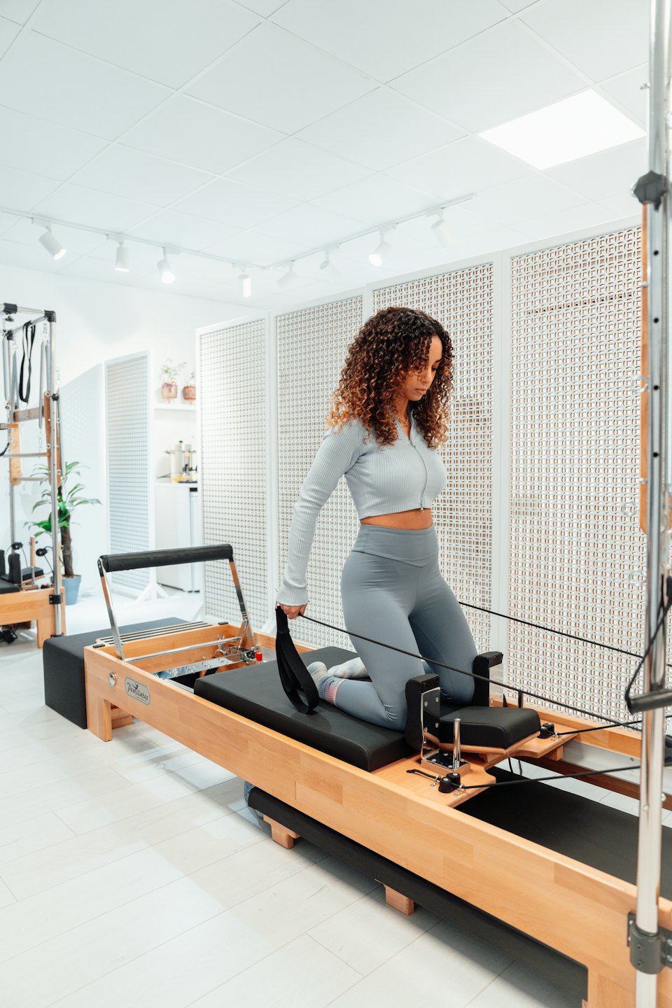Kadın ahşap bir reformer makinesinde pilates egzersizi yapıyor.